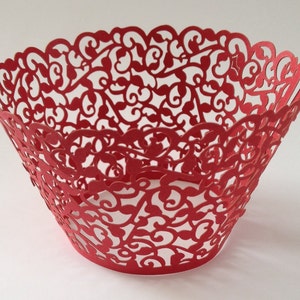 May include: A red paper bowl with a decorative, openwork design. The bowl's sides are adorned with a repeating pattern of swirling vines and leaves, and the rim has a scalloped edge. The bowl is approximately 6 inches in diameter.