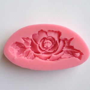 May include: Pink silicone mold with a detailed rose design. The mold is oval shaped and has a smooth surface.