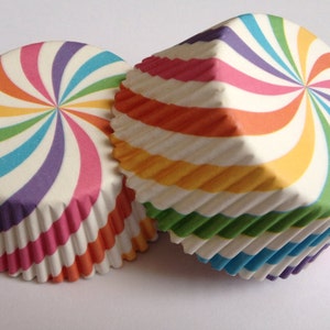 May include: Three colourful cupcake cases with a rainbow swirl pattern. The cases are made of paper and have a fluted edge.