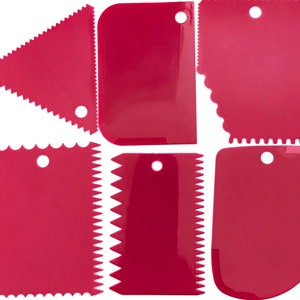May include: Set of six pink plastic cake decorating tools. The tools have different shapes and sizes, including a triangle, a rectangle, and a rounded shape. Each tool has a hole in the top for hanging.