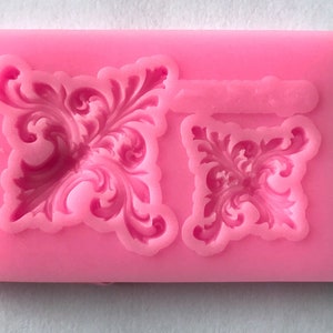 May include: Pink silicone mold with two decorative designs. The mold is for making cake decorations or other edible items.