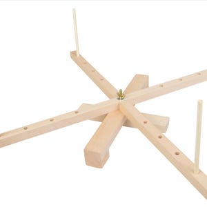 May include: A wooden yarn swift with four arms and a central spindle. Each arm has holes for winding yarn. The swift is made of natural wood and has a light brown color.
