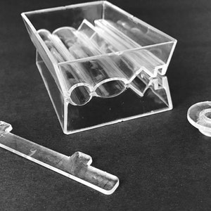 May include: A clear plastic rolling tray with three slots for rolling papers. The tray is disassembled and includes a separate lid and a small clear plastic piece.