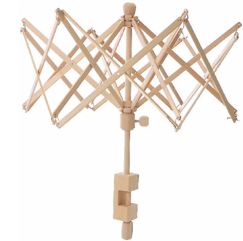 May include: A natural wood yarn swift, designed to hold yarn for winding into balls. The swift has an umbrella-like design with a clamp for attaching to a table. The wooden frame is light in color and features a series of intersecting arms.