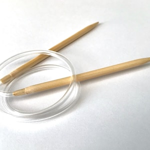 May include: A pair of bamboo knitting needles with a clear plastic cable. The needles are crossed over each other and the cable is looped around the needles.