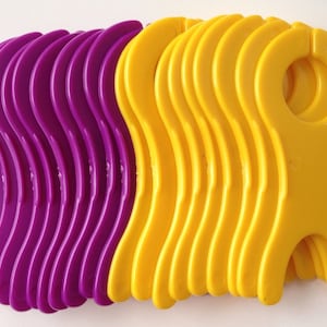 May include: A set of 10 purple and 10 yellow plastic yarn holders. The holders are shaped like a person with a loop at the top for holding yarn.