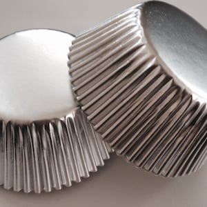 May include: Two silver cupcake liners, made of foil, with a fluted design. The liners are stacked on top of each other.