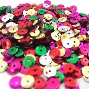 May include: A pile of colorful sequins in various shades of red, green, gold, silver, and purple. The sequins are round with a hole in the center, and they are scattered across the image.
