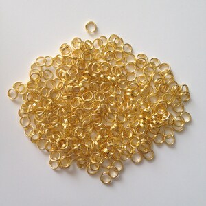 Könnte beinhalten: Ein großer Haufen goldener Sprungringe. Die Ringe sind klein und rund und liegen alle in einem Haufen.