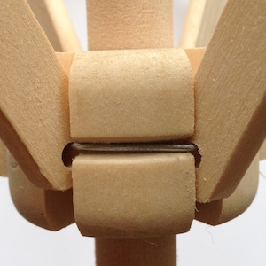 May include: Close-up of a wooden articulated artist's mannequin. The joints are held together with metal pins. The wood has a light, natural color. The mannequin is designed for posing and drawing.