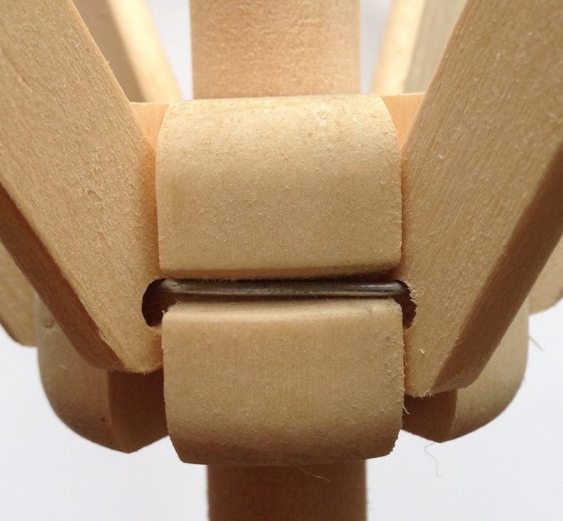 May include: Close-up of a wooden articulated artist's mannequin. The joints are held together with metal pins. The wood has a light, natural color. The mannequin is designed for posing and drawing.
