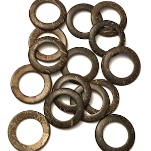 May include: A collection of dark brown, circular coconut rings with a natural, textured appearance. The rings are arranged on a white background, showcasing their organic patterns and variations in color. These rings are suitable for crafts.