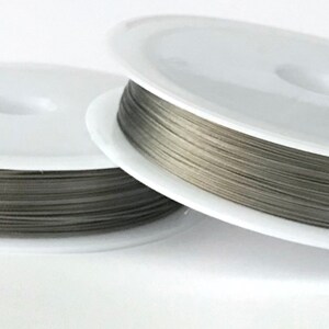 May include: Two spools of gray elastic cord, each wound around a white plastic spool.