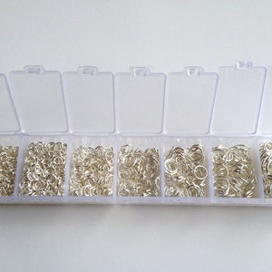 May include: A clear plastic storage box with seven compartments filled with silver jump rings.