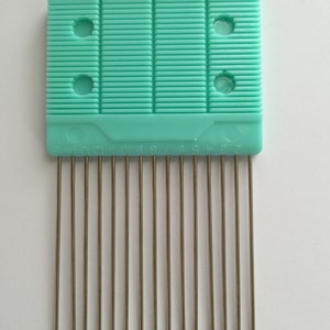 Peut inclure: Un outil de tissage en plastique turquoise avec 12 aiguilles métalliques. L'outil comporte une échelle numérotée sur le dessous, de 1 à 12.
