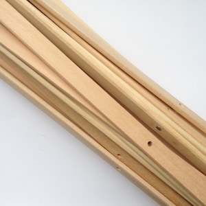 May include: A collection of unfinished wooden stretcher bars for canvas art. The bars are various widths and lengths, with a natural wood grain and small pre-drilled holes. The arrangement is diagonal against a white background.