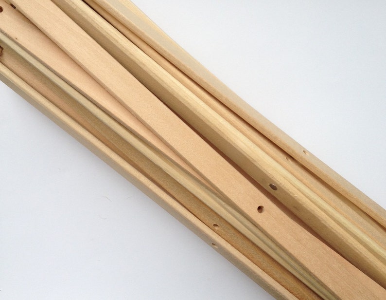 May include: A collection of unfinished wooden stretcher bars for canvas art. The bars are various widths and lengths, with a natural wood grain and small pre-drilled holes. The arrangement is diagonal against a white background.