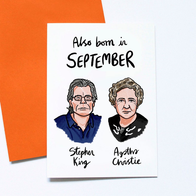 May include: A white greeting card with the text "Also born in SEPTEMBER" and illustrations of Stephen King and Agatha Christie. The card is paired with an orange envelope.