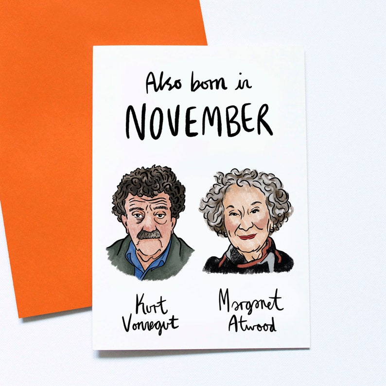 May include: A white greeting card with the text "Also born in NOVEMBER" above illustrations of Kurt Vonnegut and Margaret Atwood. The card is paired with an orange envelope. The names of the authors are written below their portraits.