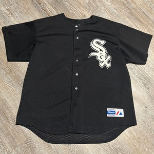 May include: Black baseball jersey with a white Chicago White Sox logo on the left chest. The jersey has a button-up front and a Majestic Apparel tag on the bottom right.