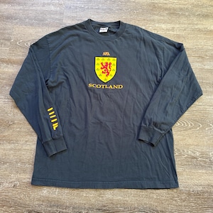 Peut inclure: T-shirt &agrave; manches longues gris fonc&eacute; avec l'embl&egrave;me de l'&Eacute;cosse. L'embl&egrave;me est un &eacute;cusson jaune avec un lion rouge et le mot "SCOTLAND" en jaune. La manche gauche a des rayures jaunes. Le t-shirt est en mati&egrave;re souple.
