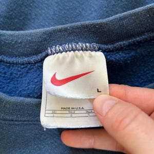 May include: A blue Nike sweatshirt with a white tag that says "Made in U.S.A." and has the size "L" printed on it.