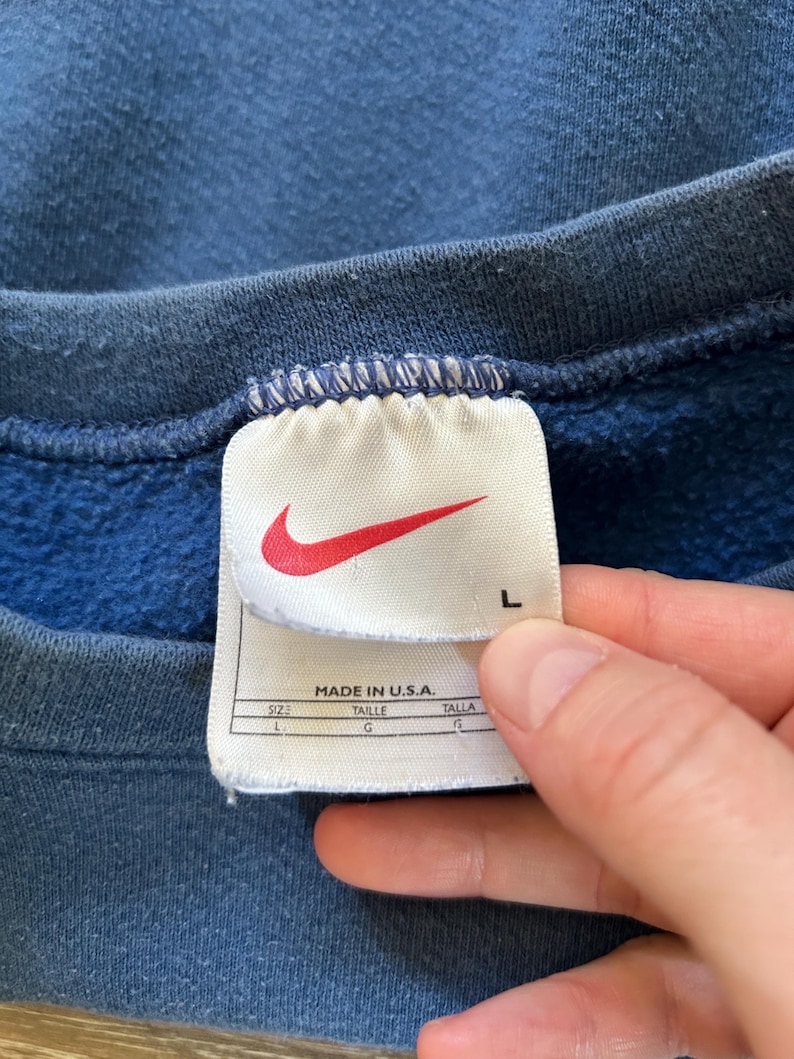 May include: A blue Nike sweatshirt with a white tag that says "Made in U.S.A." and has the size "L" printed on it.