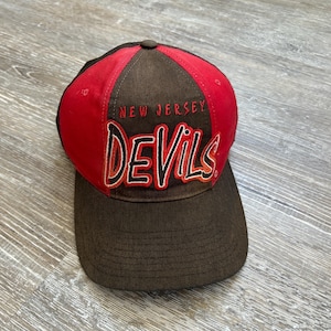 May include: A red and brown baseball cap with the words "New Jersey Devils" embroidered on the front.