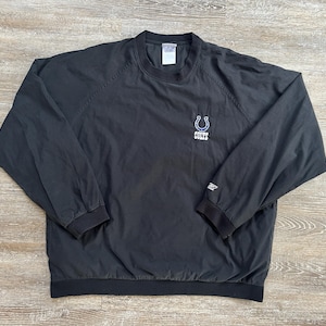 May include: Black pullover windbreaker with the Indianapolis Colts logo embroidered on the chest. The logo features a blue horseshoe with the word "Colts" underneath. The windbreaker has a crew neck and elastic cuffs.