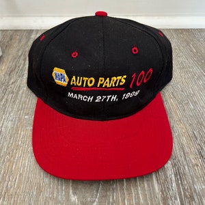 May include: Black and red baseball cap with the text "NAPA AUTO PARTS 100 MARCH 27TH, 1999" embroidered on the front.