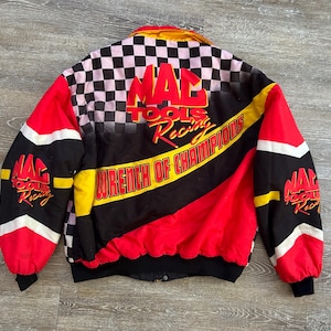 May include: A vintage racing jacket with a black, red, and white color scheme. The jacket features the text "MAC TOOLS Racing Wrench of Champions" across the front and back. The upper back has a checkered pattern.