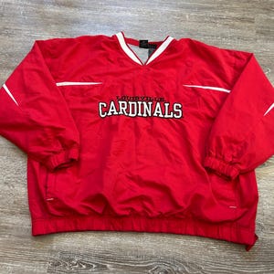 May include: Red Louisville Cardinals pullover jacket with white accents. Features a V-neck collar with white trim and the team name in white lettering. The jacket has a drawstring hem and elastic cuffs.
