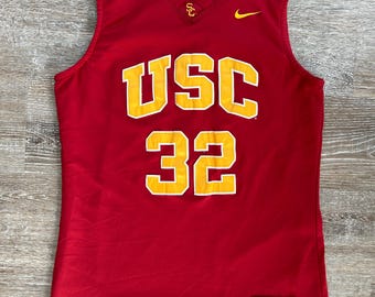 May include: Red basketball jersey with the letters "USC" and the number "32" in yellow. The Nike logo is on the right shoulder and the jersey has a size tag that says "M".