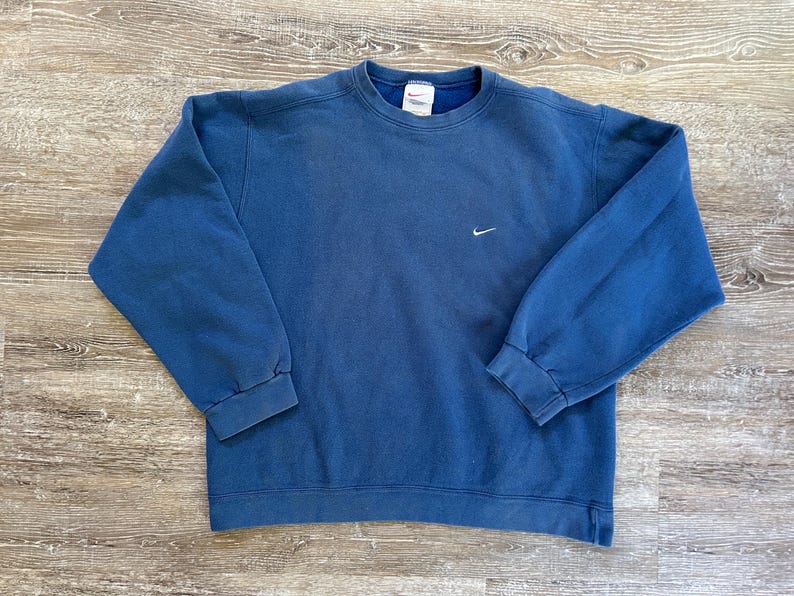May include: A blue crew neck sweatshirt with a white Nike swoosh logo on the front.