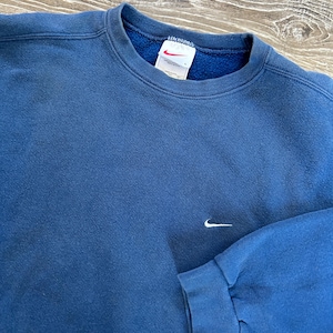 May include: A blue sweatshirt with a white Nike logo on the front. The sweatshirt has a crew neck and long sleeves.