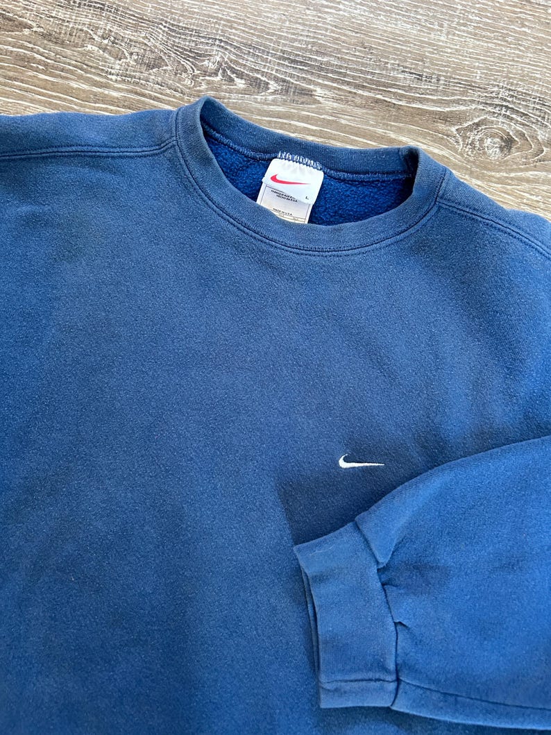 May include: A blue sweatshirt with a white Nike logo on the front. The sweatshirt has a crew neck and long sleeves.