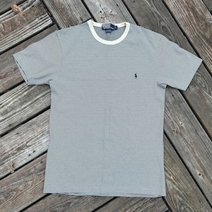 Puede incluir: Camiseta a rayas azul marino y blancas con cuello redondo color crema. La camiseta presenta un pequeño logotipo azul marino en el pecho izquierdo. La camiseta de manga corta está hecha de una tela suave y transpirable.