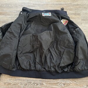 Pode incluir: Uma caneca de cer&acirc;mica branca com uma al&ccedil;a preta e o texto "But First, Coffee" em preto, em negrito. A caneca est&aacute; sobre uma superf&iacute;cie branca.