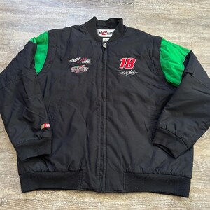 May include: Black zip-up jacket with green shoulder accents. Features the number 18 in red, along with racing-themed logos and text. The jacket has a ribbed collar, cuffs, and hem. A Champion brand label is visible.