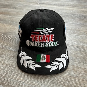 May include: Black baseball cap featuring the Tecate and Quaker State logos with a checkered flag design. The cap has a Mexican flag patch and white leaf embroidery on the brim.