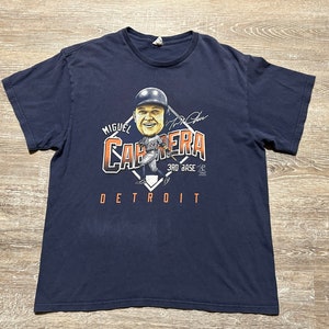 May include: A navy blue t-shirt with a cartoon image of baseball player Miguel Cabrera. The shirt features the text "Miguel Cabrera 3rd Base Detroit" and a signature.