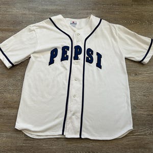 May include: White baseball jersey with navy blue trim and the word "PEPSI" in navy blue block letters across the chest. The jersey has a button-up front and short sleeves.