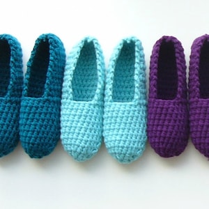May include: Five pairs of crocheted slippers in shades of teal, light blue, and purple. The slippers are all the same style, with a simple, rounded toe and a flat sole.