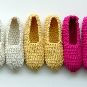 Può includere: Cinque paia di pantofole all'uncinetto in diversi colori. Le pantofole sono bianche, gialle e rosa.