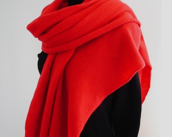 May include: A vibrant red scarf draped over a black top. The scarf is made of a soft, textured material and is wrapped around the neck and shoulders. The bright color of the scarf contrasts with the dark clothing.