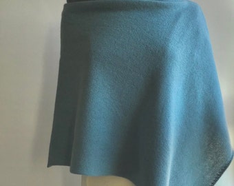 May include: A teal-colored poncho-style wrap made of soft fabric. The wrap is draped over a mannequin, showcasing its shape and texture. The garment has a wide neckline and a flowing, asymmetrical hemline, suitable for layering.