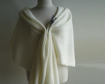 May include: Cream-colored shawl draped over a mannequin, with a lavender sprig pinned at the front. The shawl is made of a soft, flowing fabric, with folds and drapes that create a sense of elegance. The overall aesthetic is simple and refined.