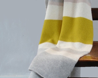 May include: A gray and white striped throw blanket with a yellow stripe draped over a wooden chair.