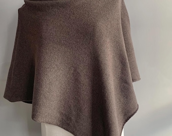 Puede incluir: Un poncho marrón con cuello alto, exhibido en un maniquí. El poncho está hecho de una tela suave y texturizada. La prenda tiene un dobladillo asimétrico y fluido y se drape sobre los hombros.
