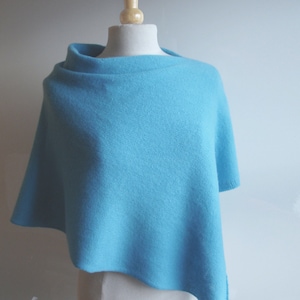 Pode incluir: Um poncho de malha azul claro com decote drapeado.